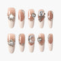 Elegant nude press-on nails with glossy finish, rhinestone and pearl embellishments, and 3D gems.