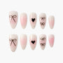 Pink and nude press-on nails with black bow and heart designs, speckled accents