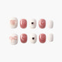 Handmade pink and white press-on nails with glitter, heart and bow designs, arranged on a white background.