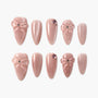 Set of pink press-on nails with 3D bow designs and rhinestone accents on a white background