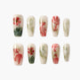 Handmade press-on nails with red floral and green leaf designs on a pale background