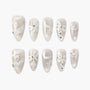 Handmade press-on nails with pearly white base, white swirl designs, and rhinestone accents