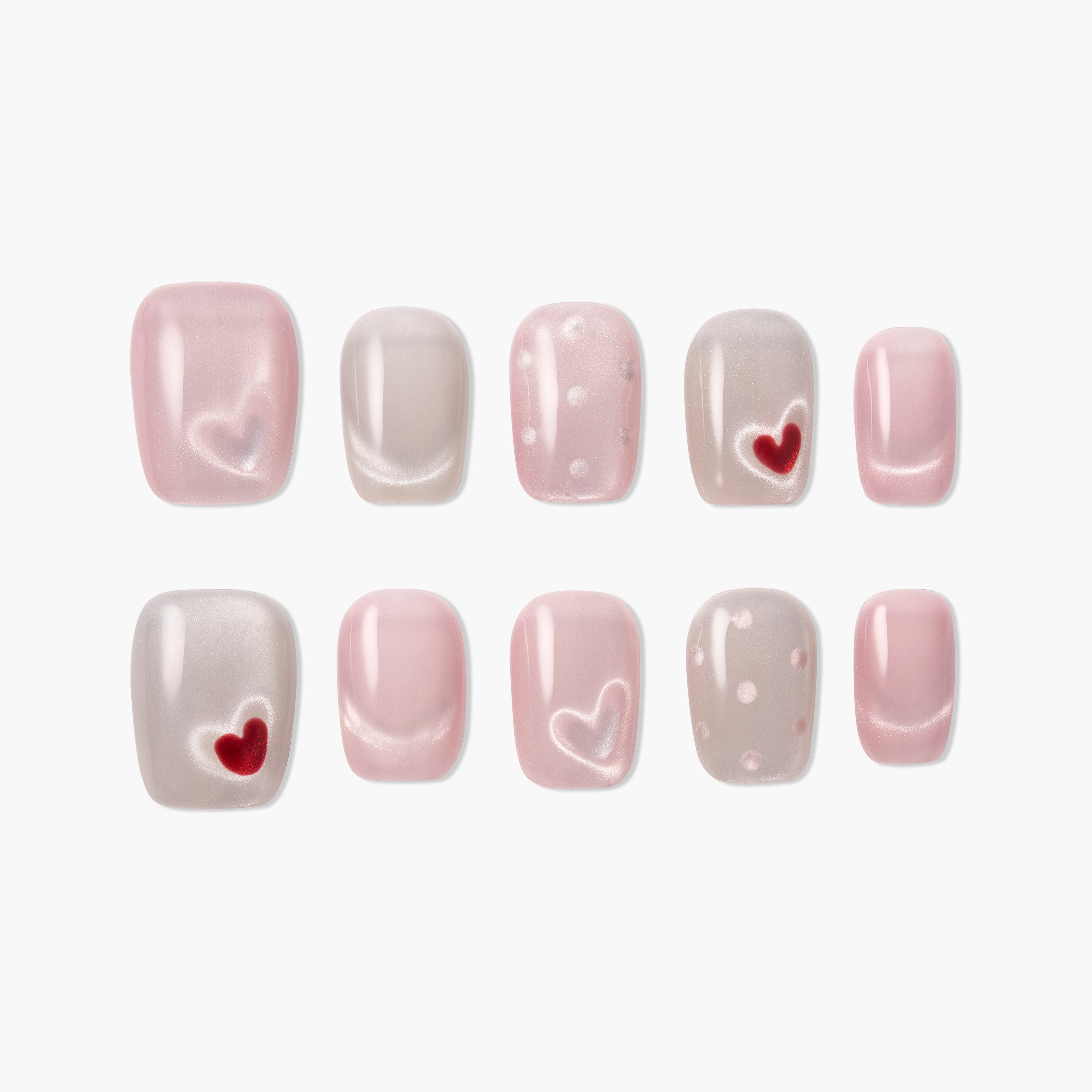 Set of pink and nude press-on nails with heart and polka dot designs on white background