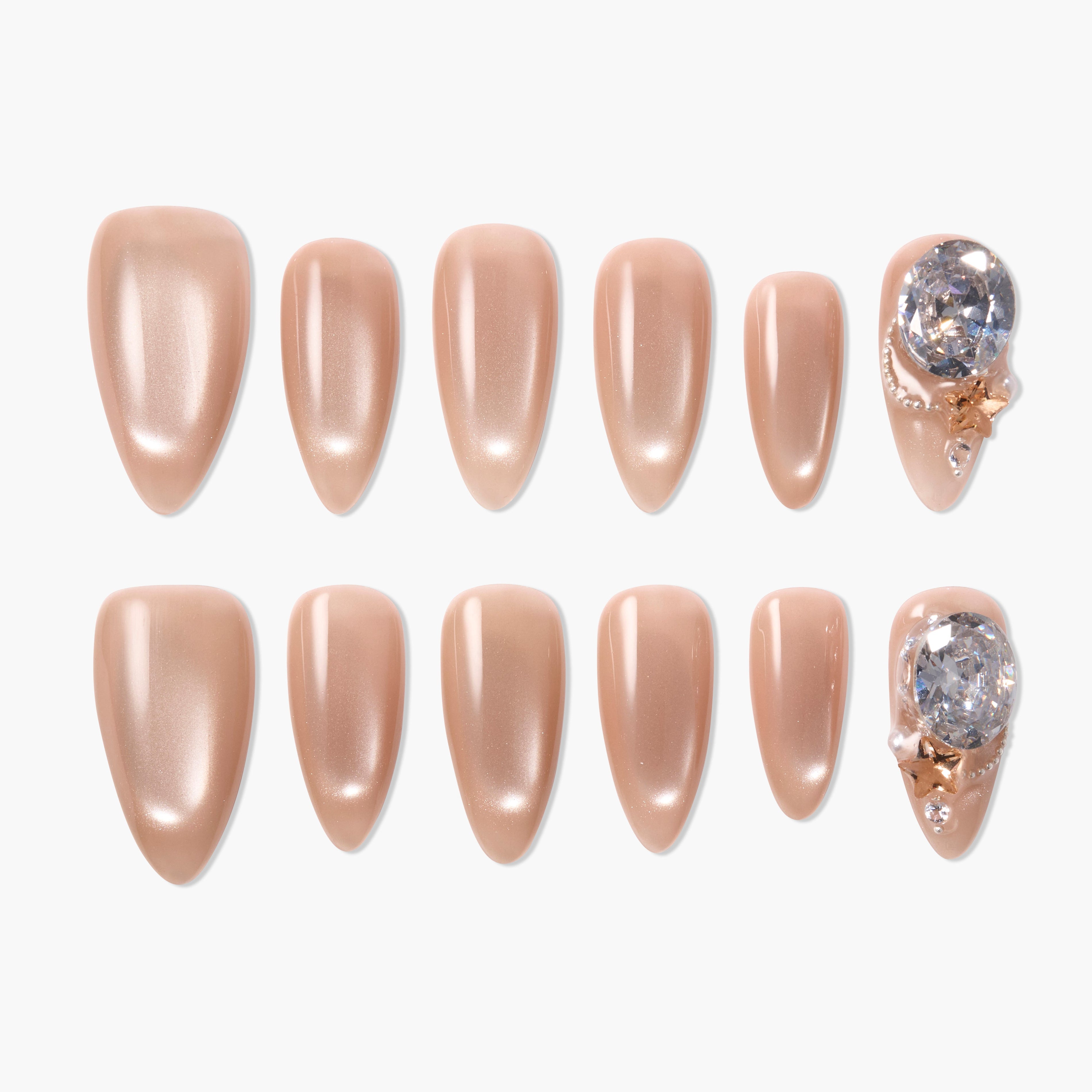 Nude press-on nails set with glossy finish and two accent nails featuring large rhinestones and gold stars.