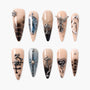 Handmade press-on nails with nude and black ombre, metallic silver charms, and gothic designs.