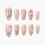 Handmade press-on nails with nude base and pink floral designs, arranged on white background.