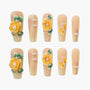 Handmade press-on nails with yellow 3D floral designs, pearls, and green leaf accents