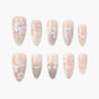 Handmade press-on nails in soft pink with white floral, leaf, and bow nail art designs.