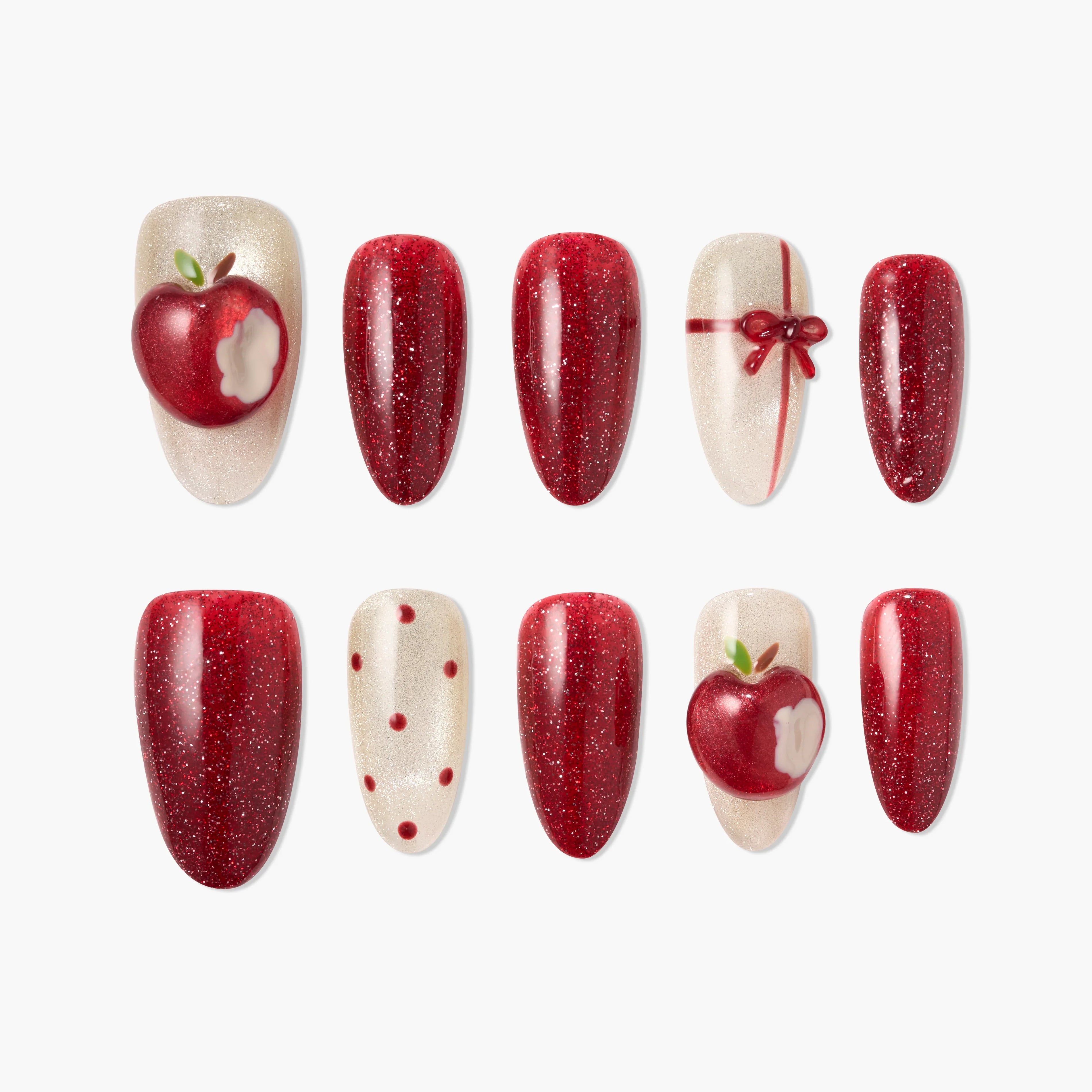 Red and glittery press-on nails with apple and bow designs, polka dots, and bite accents.