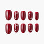 Set of glossy red press-on nails with rhinestone accents, arranged on a white background.
