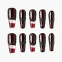 Glossy red and black press-on nails with glitter and black textured accents, arranged in two rows.