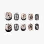 Handmade press-on nails with black abstract designs, rhinestone accents, and nude bases.