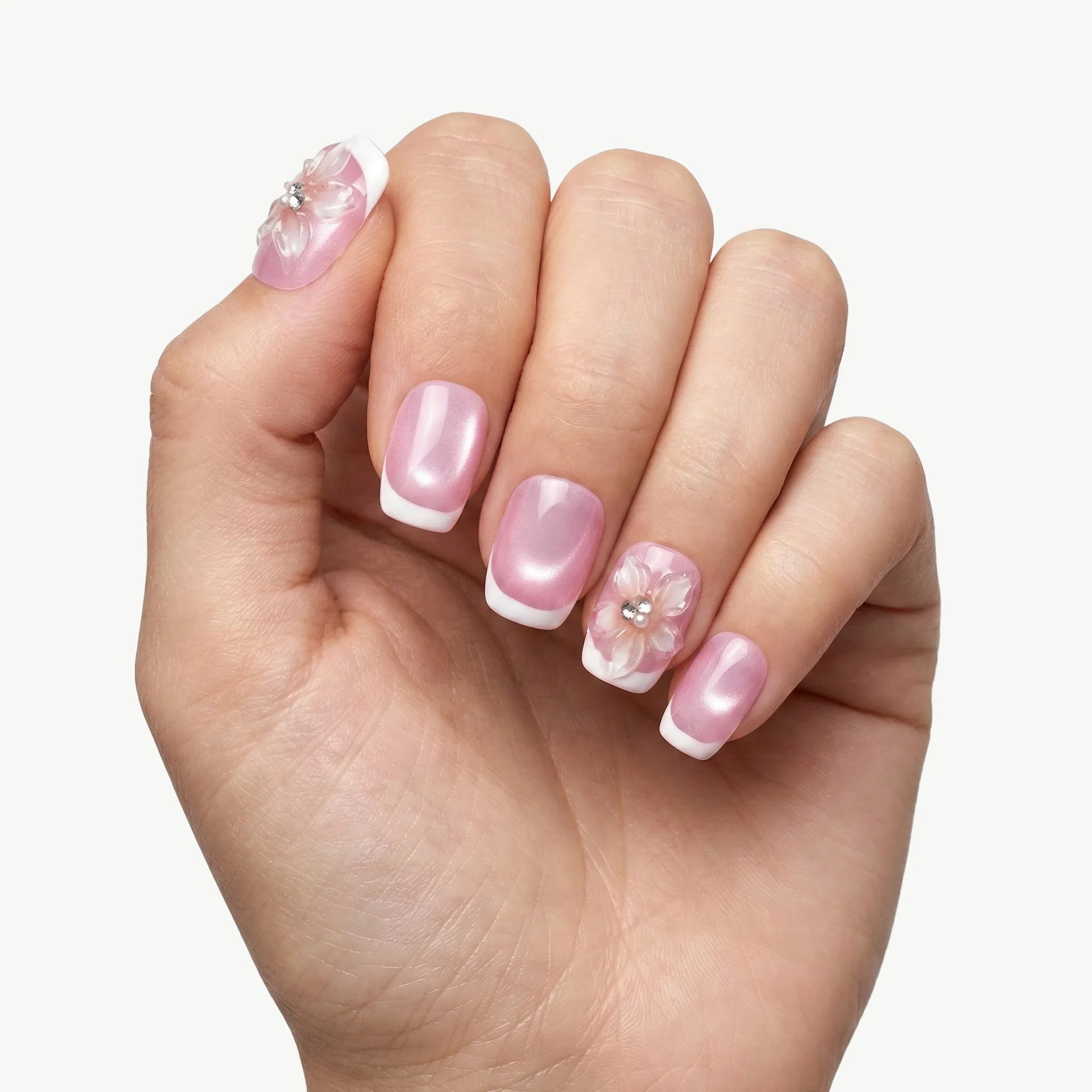 Hand with pink French tip press-on nails featuring 3D floral and rhinestone accents
