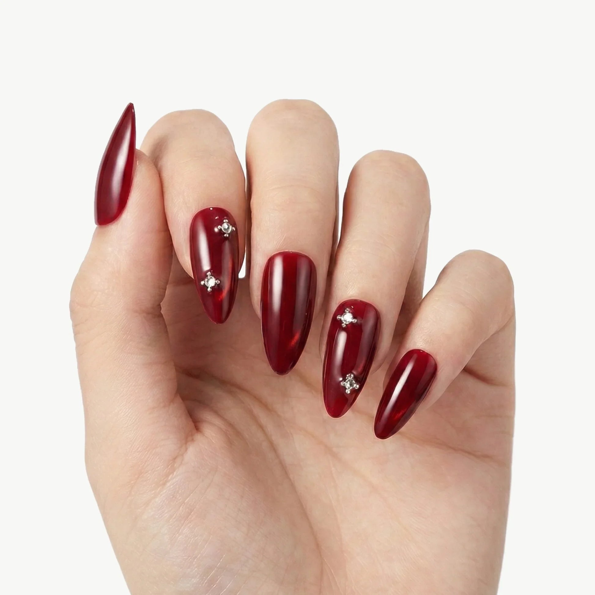 Hand with long almond-shaped red press-on nails with rhinestone accents