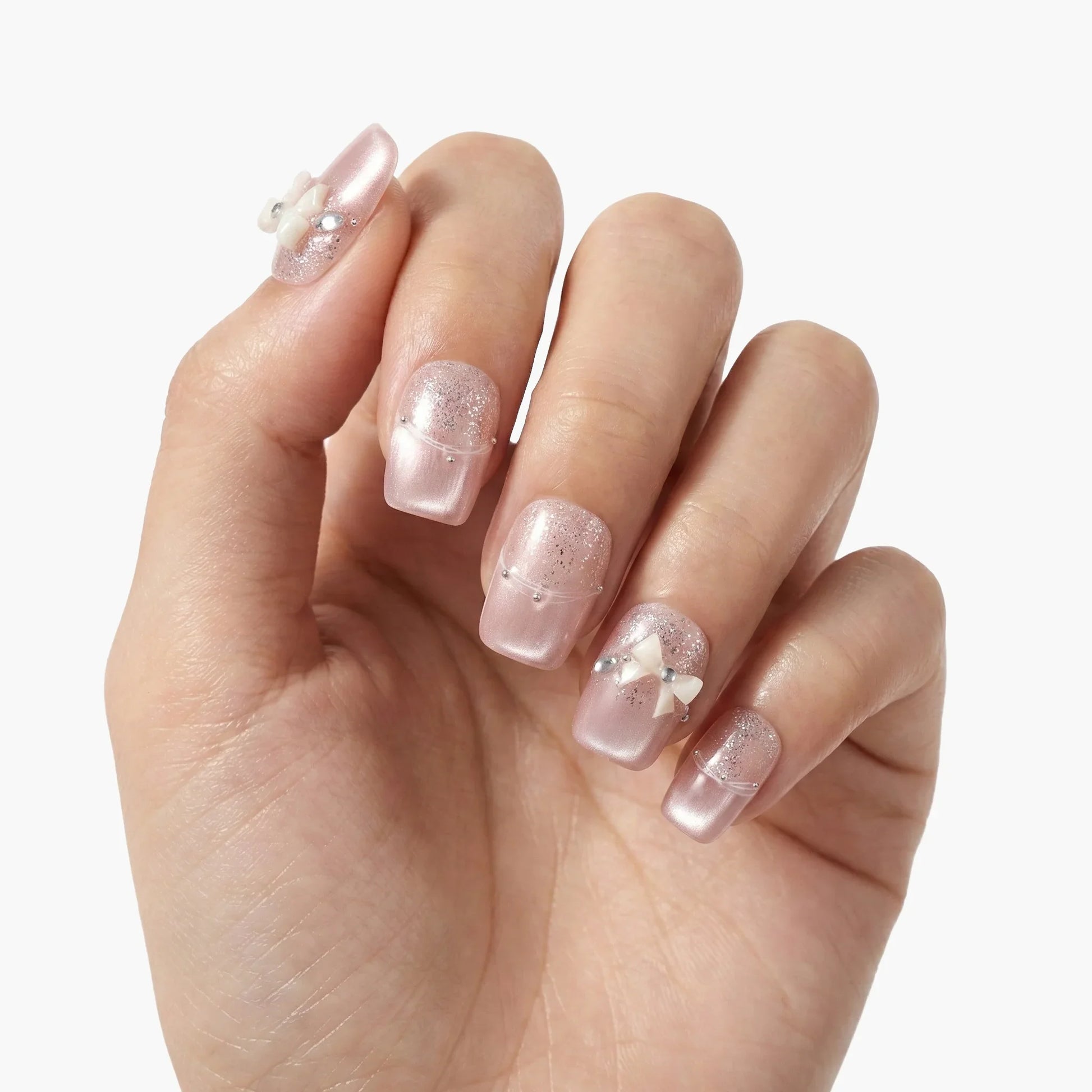 Hand with pink glitter press-on nails featuring rhinestones and 3D bow nail art