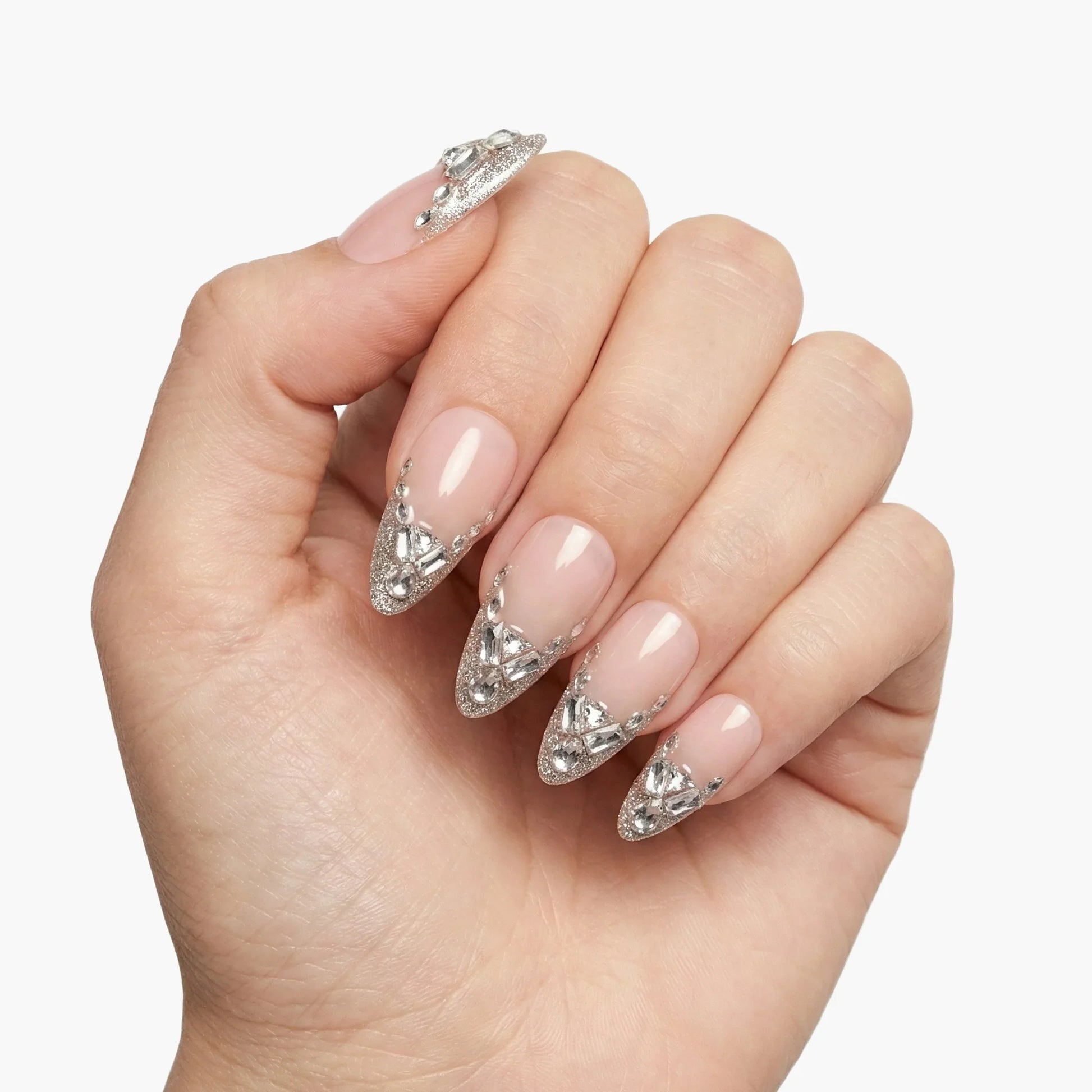 Hand displaying almond-shaped press-on nails with silver rhinestone accents on nude base
