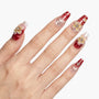 Hand with red and nude ombre press-on nails, 3D floral accents, and rhinestone details
