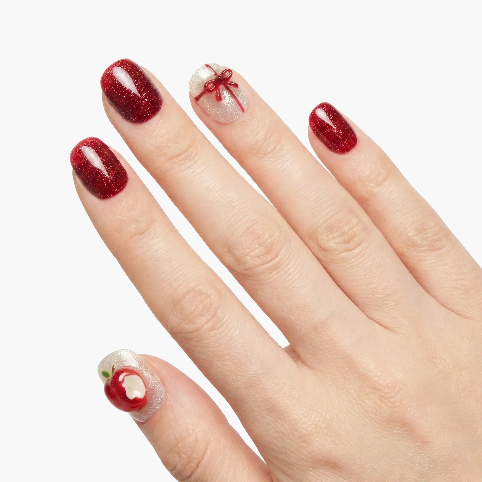 Hand with red glitter press-on nails, white accent nails with apple and bow designs