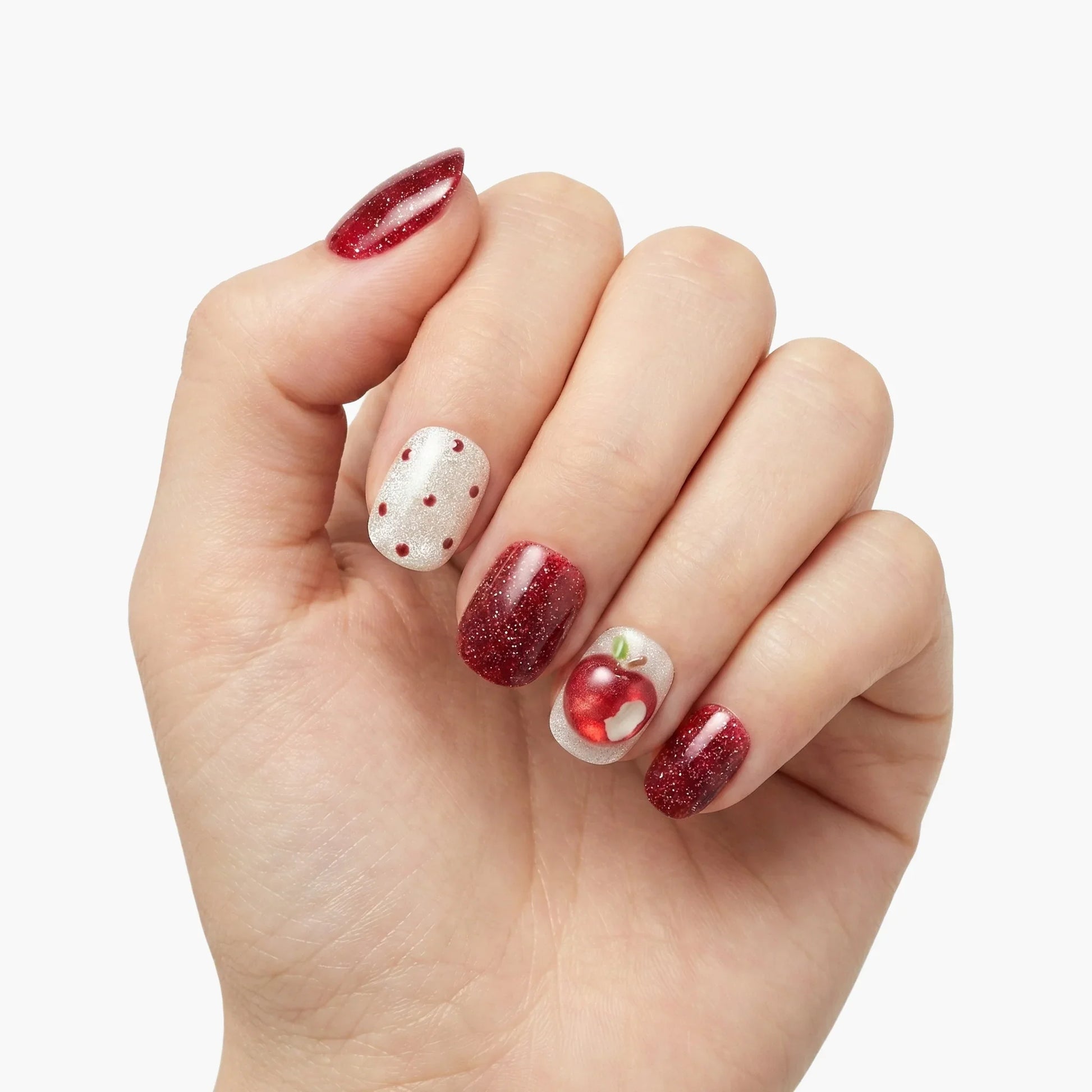 Hand with red glitter press-on nails, white polka dot accent, and apple nail art design