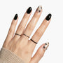 Hand with black press-on nails and nude accent nails featuring black floral designs