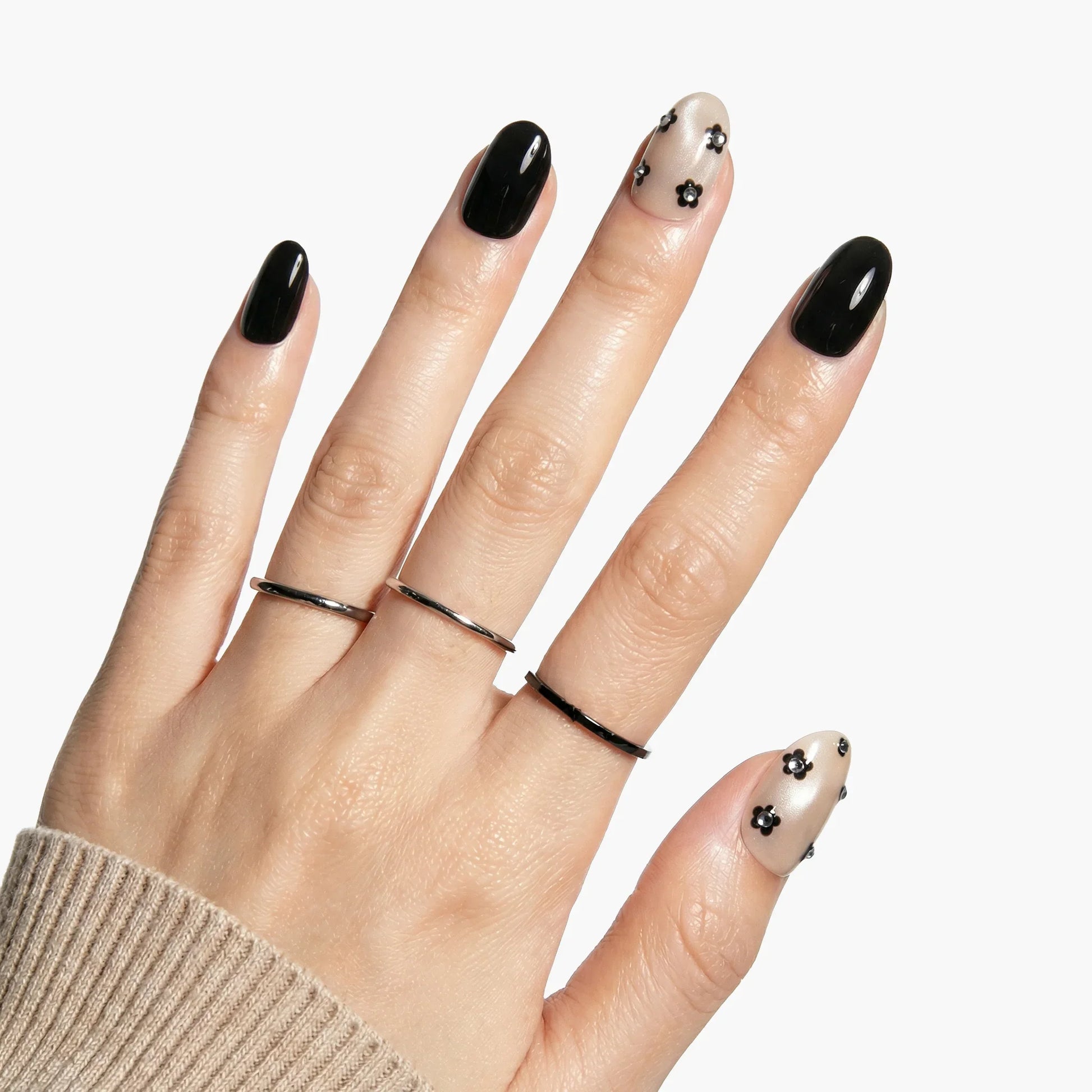 Hand with black press-on nails and nude accent nails featuring black floral designs