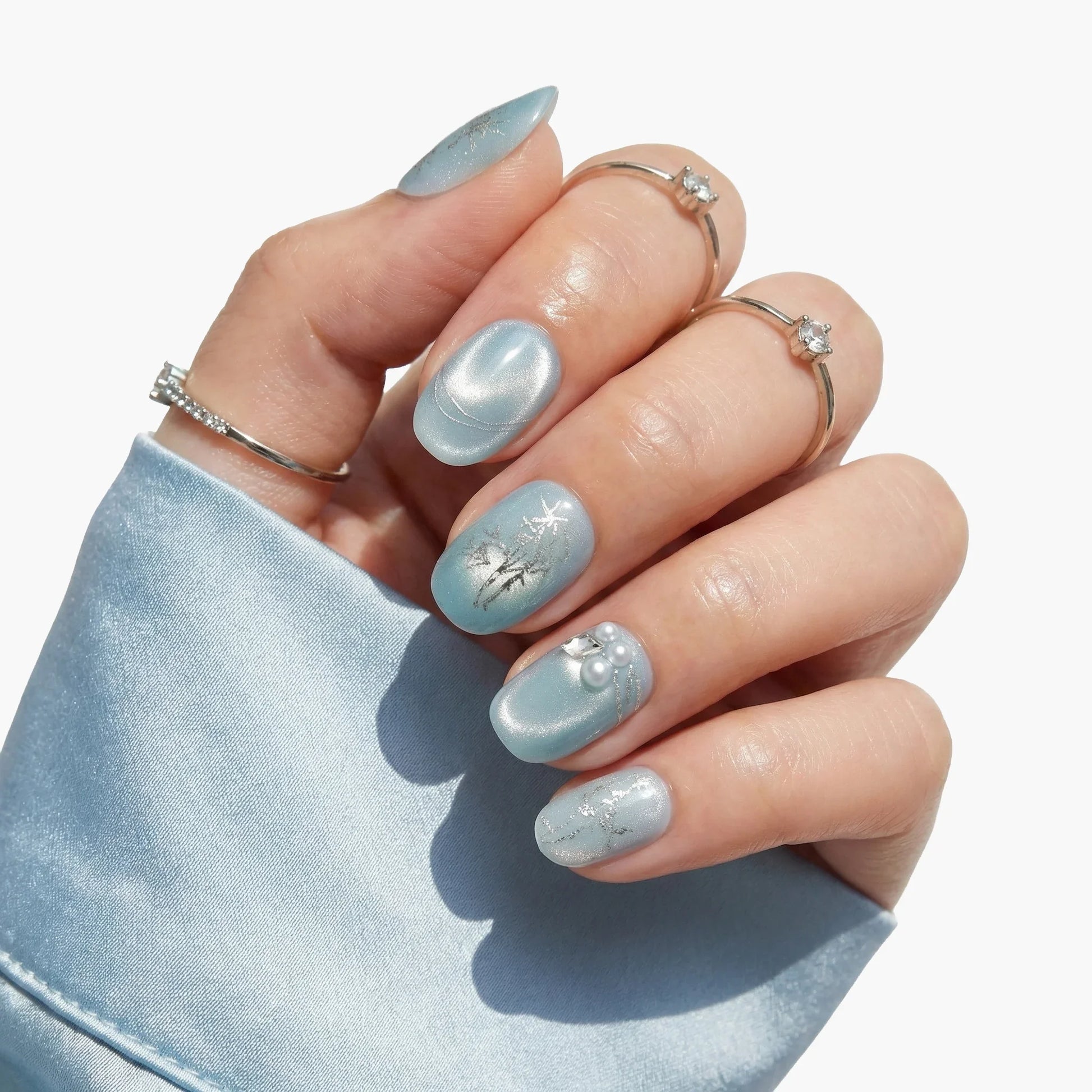 Hand with light blue press-on nails featuring winter snowflake art and pearl accents