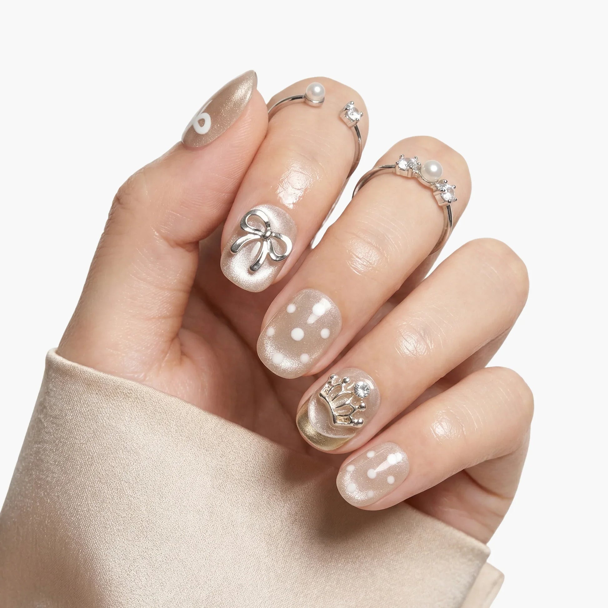 Hand with pearl nude press-on nails, 3D bow and crown accents, and white dot designs