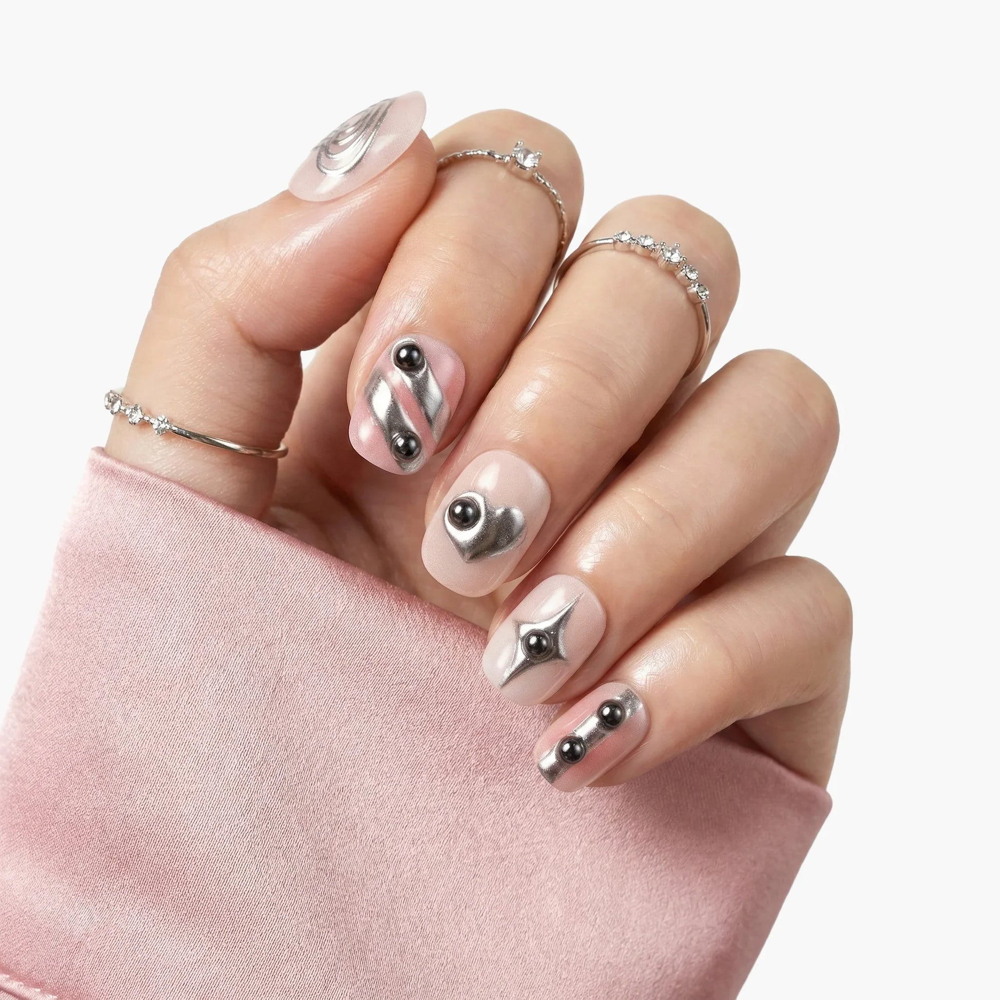 Hand with silver metallic press-on nails featuring 3D accents and geometric designs