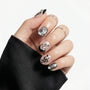 Hand with silver and black press-on nails, featuring abstract nail art and pearl accents