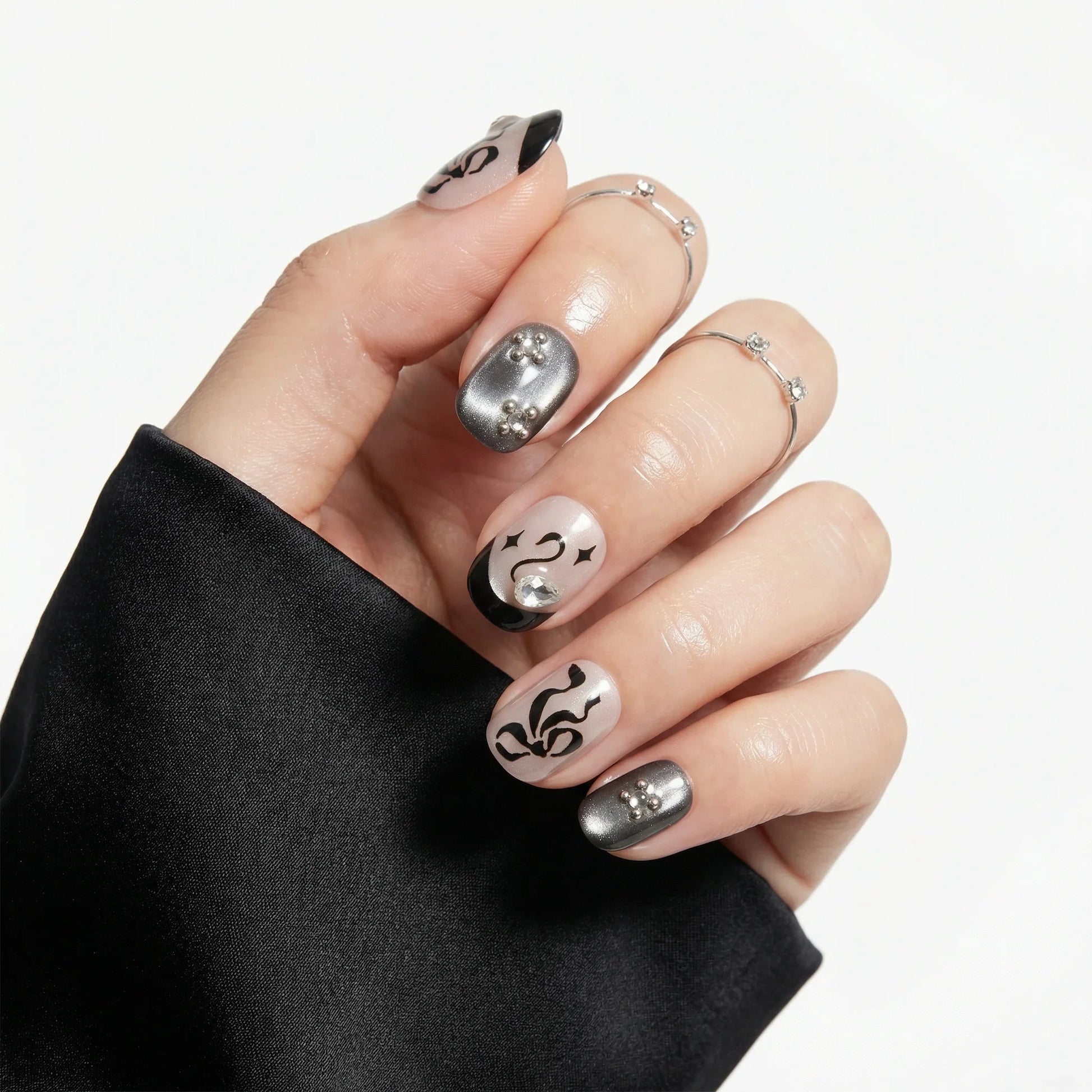 Hand with silver and black press-on nails, featuring abstract nail art and pearl accents