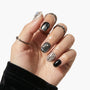 Hand with black, gray, and silver press-on nails featuring marble and metallic designs.