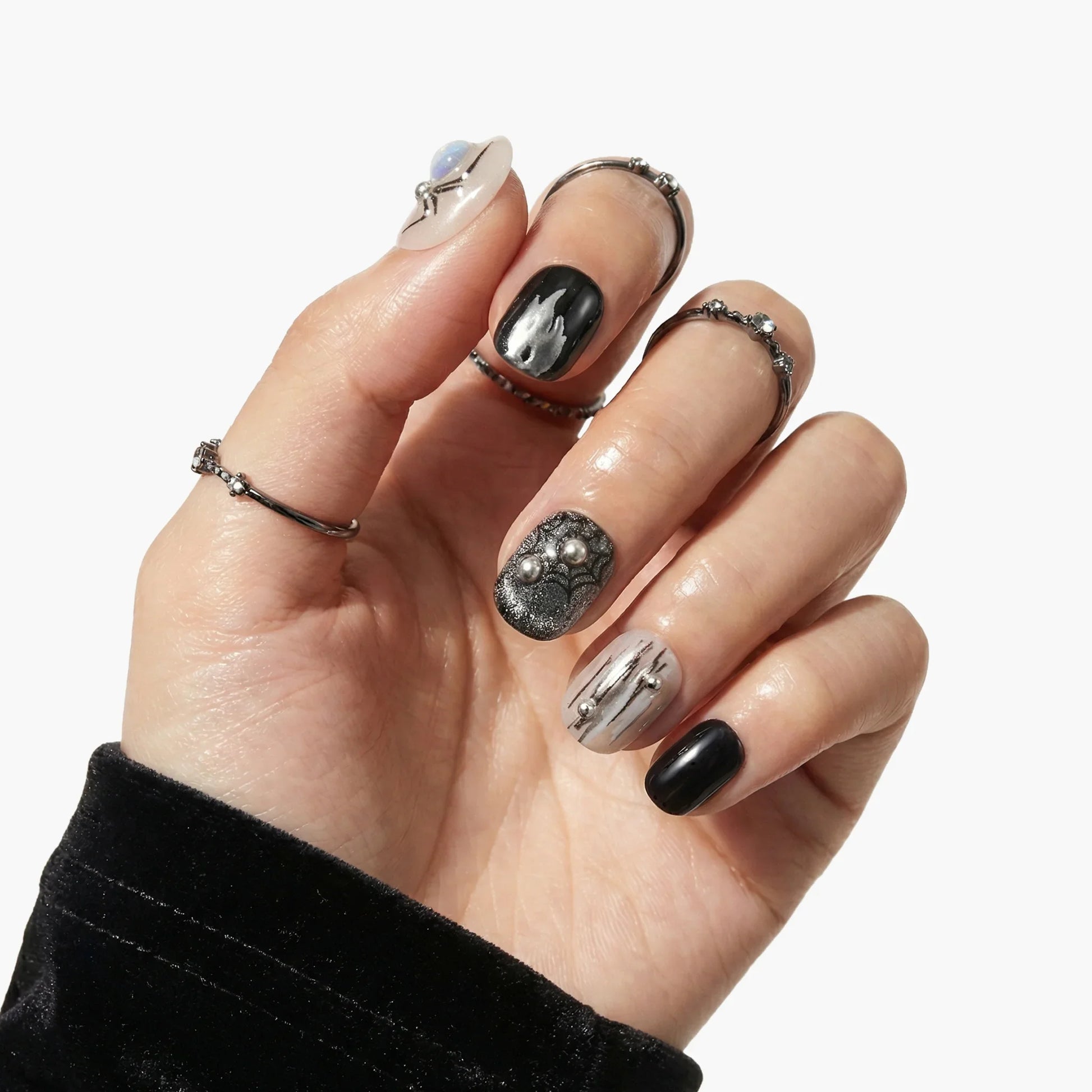 Hand with black, gray, and silver press-on nails featuring marble and metallic designs.