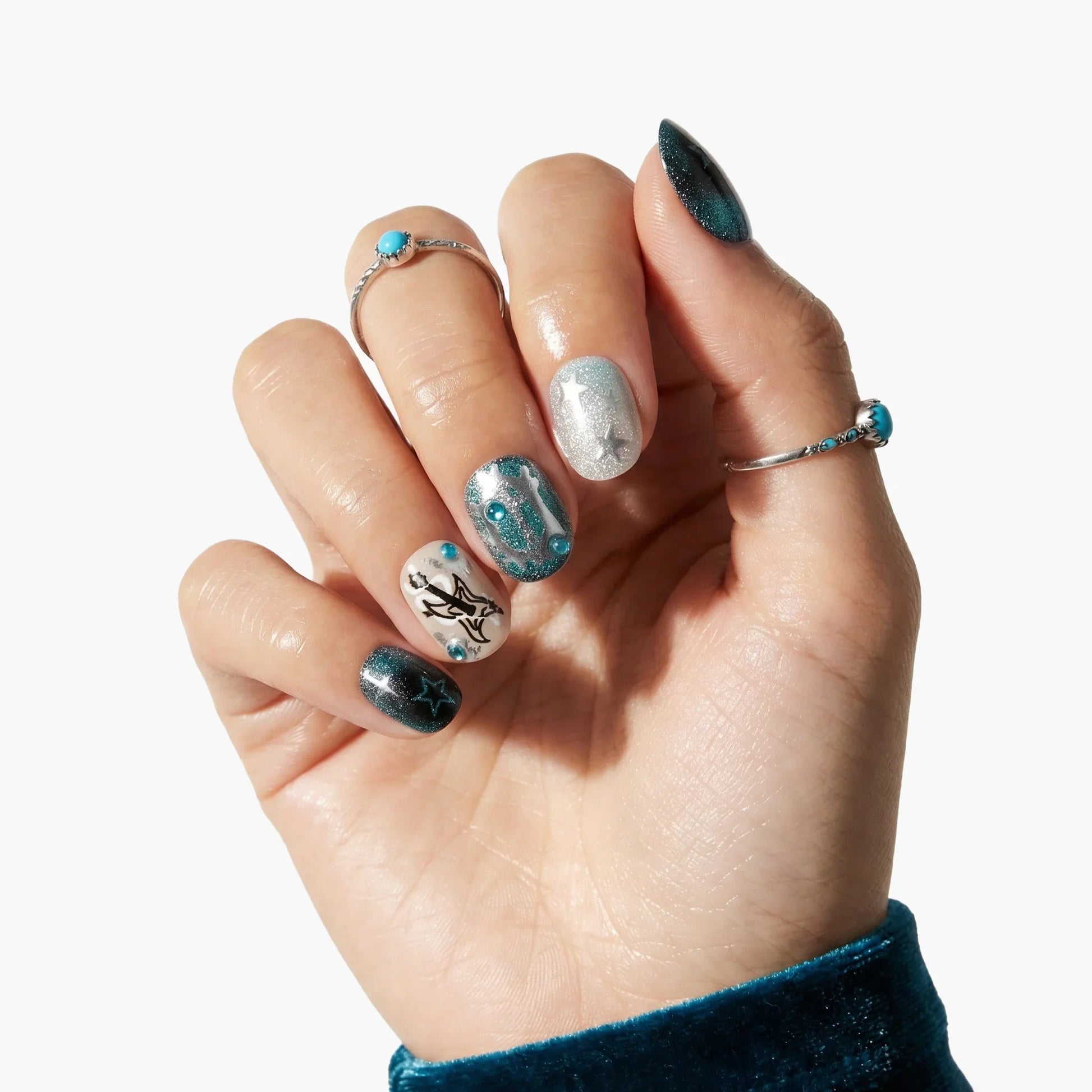 Hand with premium press-on nails featuring metallic blue, silver, and star designs