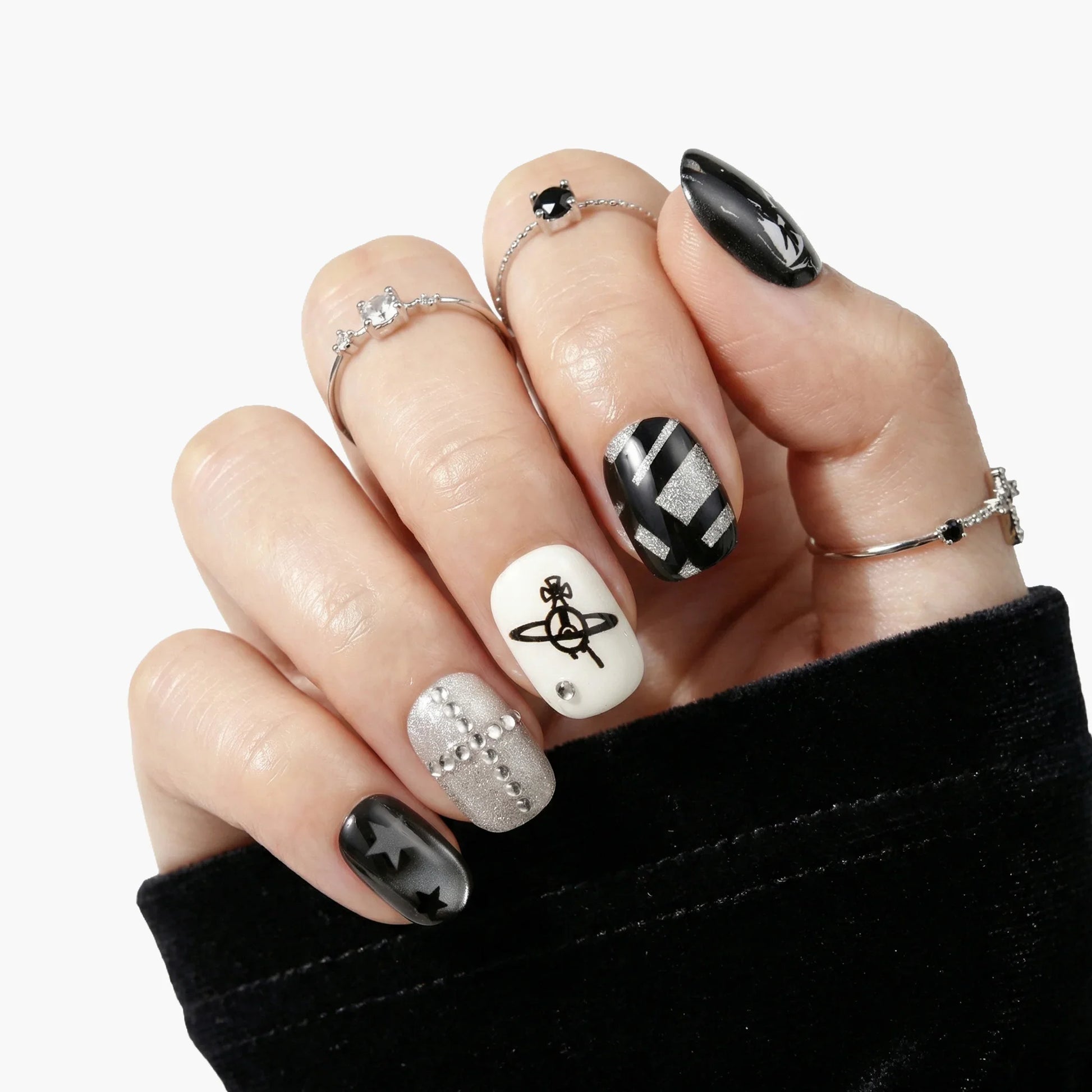Hand with black, silver, and white press-on nails featuring stars, stripes, and cross designs