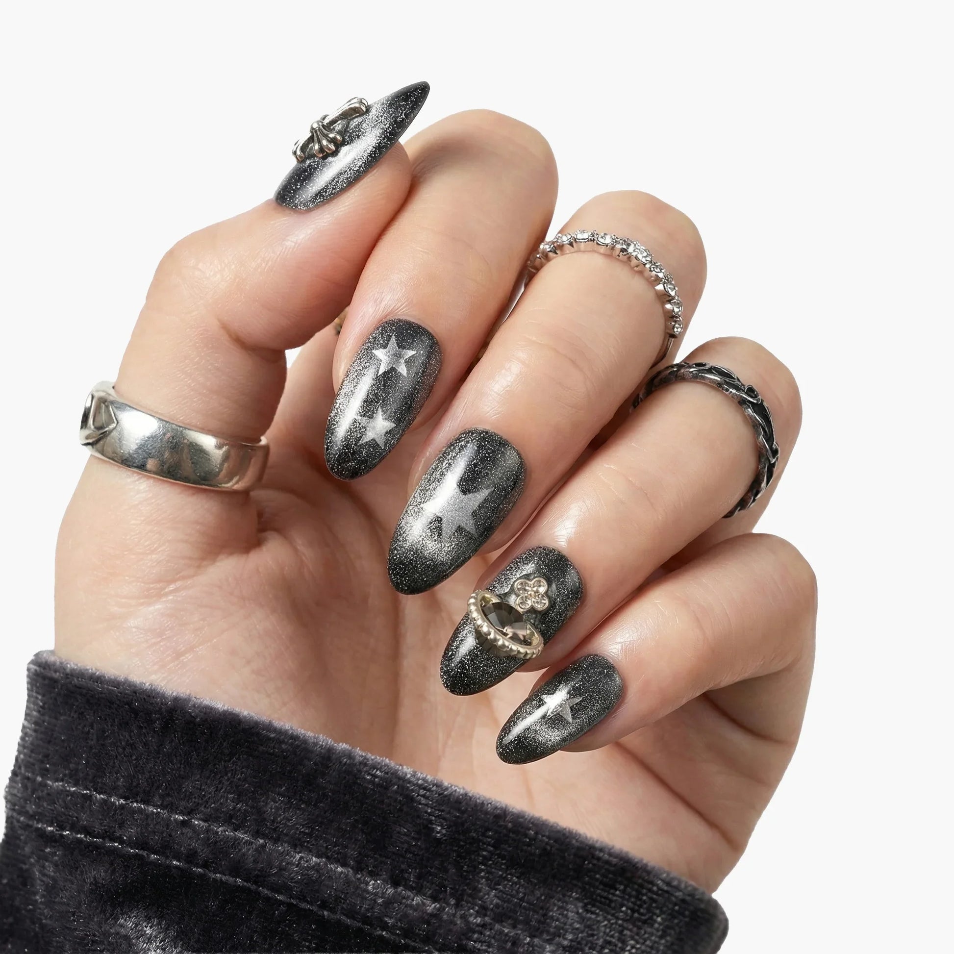 Hand with black star-themed press-on nails and silver rings, showcasing manicure style.