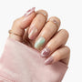 Hand with pastel iridescent press-on nails and gold rings, soft pink sleeve background