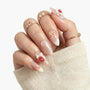 Hand with long almond-shaped press-on nails, pink and white with 3D strawberry and bow designs, pearl rings.
