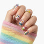 Hand with colorful star and stripe press-on nails, wearing rainbow ring and sweater.