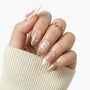 Hand with almond-shaped press-on nails featuring gold glitter tips, 3D bows, and pearl accents