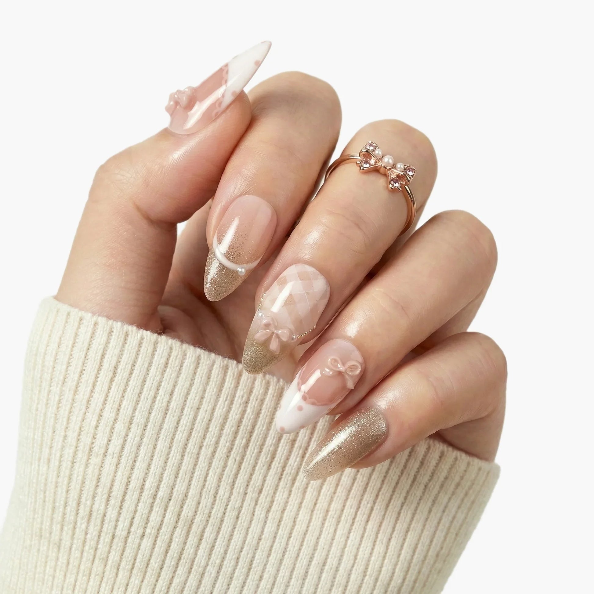 Hand with almond-shaped press-on nails featuring gold glitter tips, 3D bows, and pearl accents