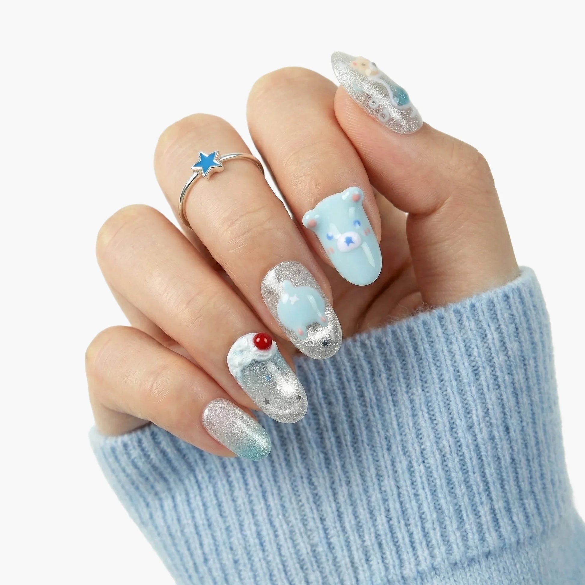 Hand with blue and silver press-on nails featuring 3D bear, penguin, and star designs