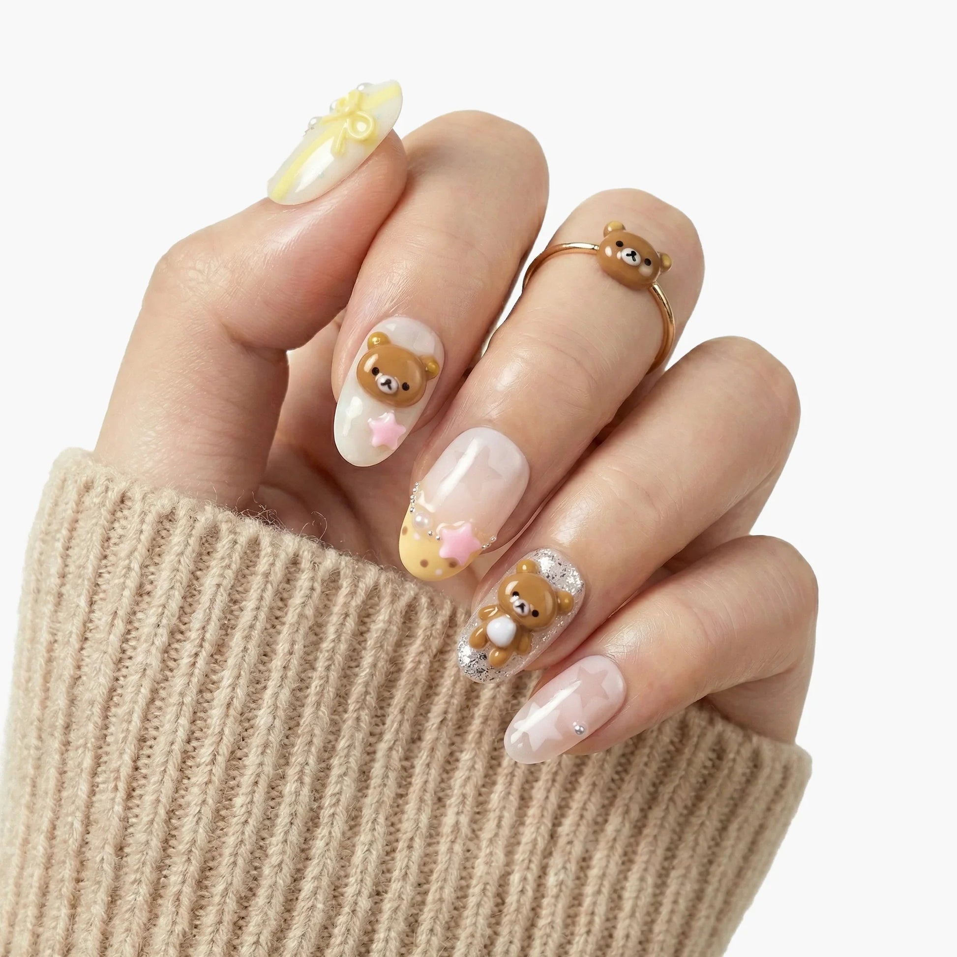 Hand with pastel press-on nails featuring 3D bear, stars, dots, and pearl nail art accents