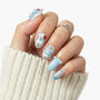Hand with blue and silver press-on nails featuring 3D bear and star designs, cozy sweater