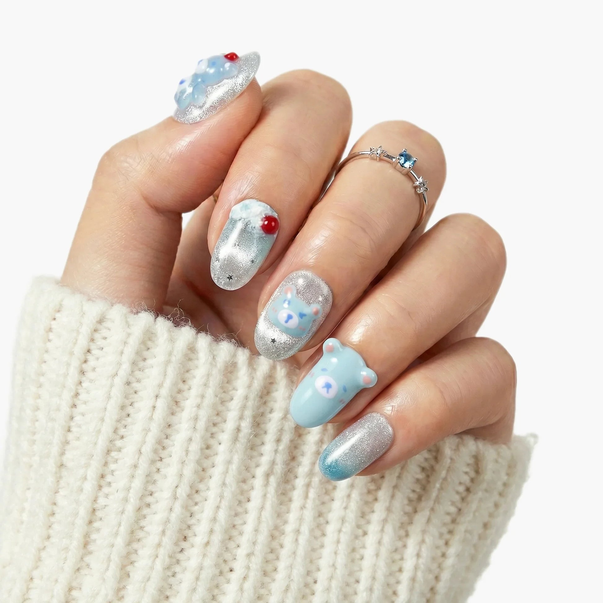 Hand with blue and silver press-on nails featuring 3D bear and star designs, cozy sweater