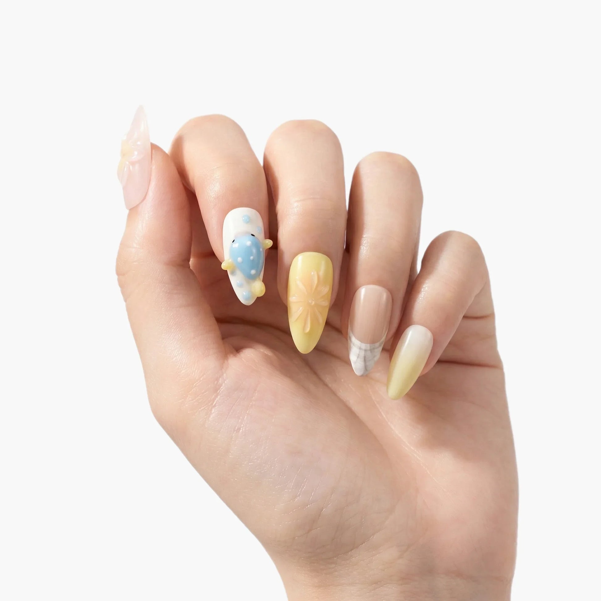 Hand showing long press-on nails with pastel yellow, 3D floral, blue polka dot, and plaid designs