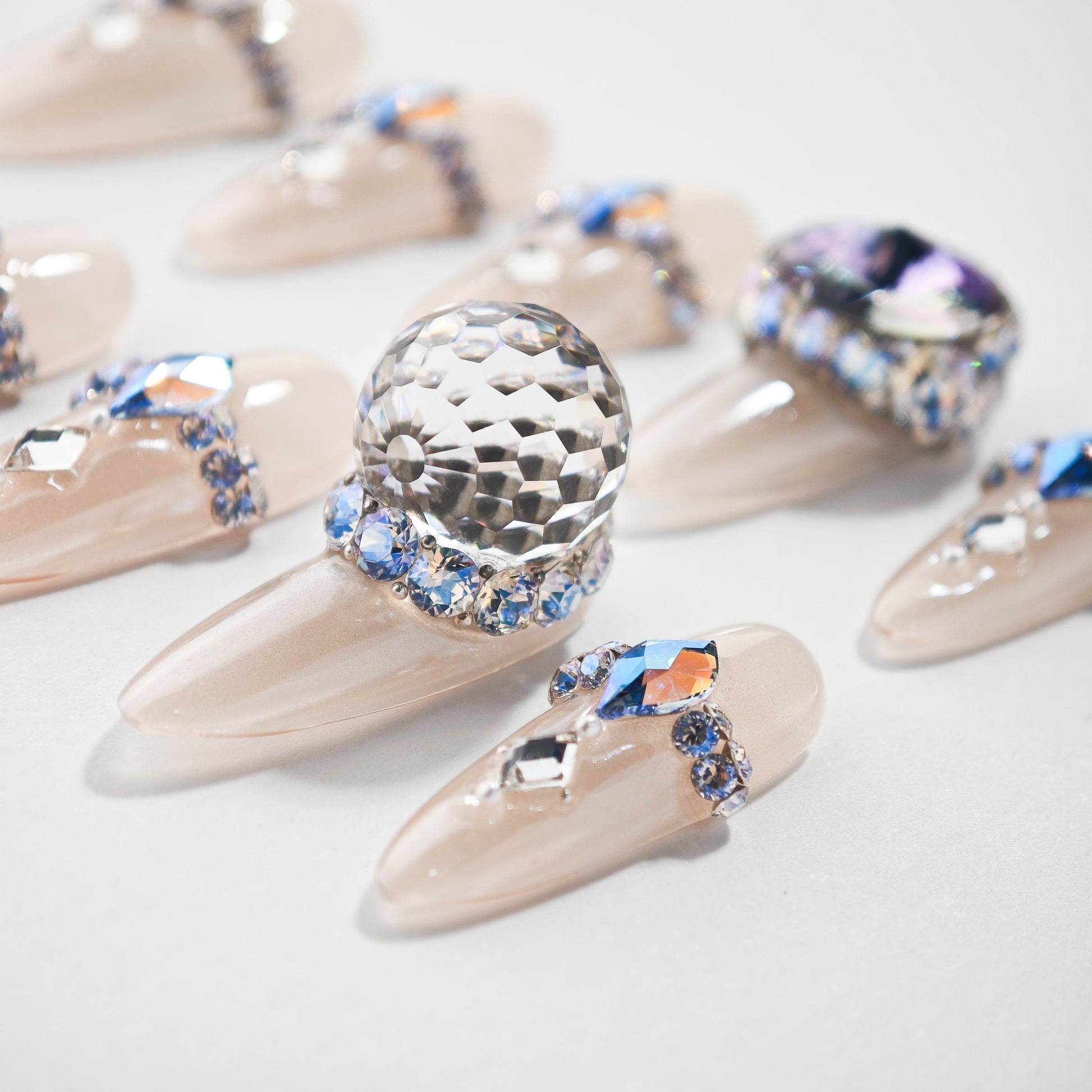 Glossy nude press-on nails with large crystal and blue rhinestone accents, luxury nail art