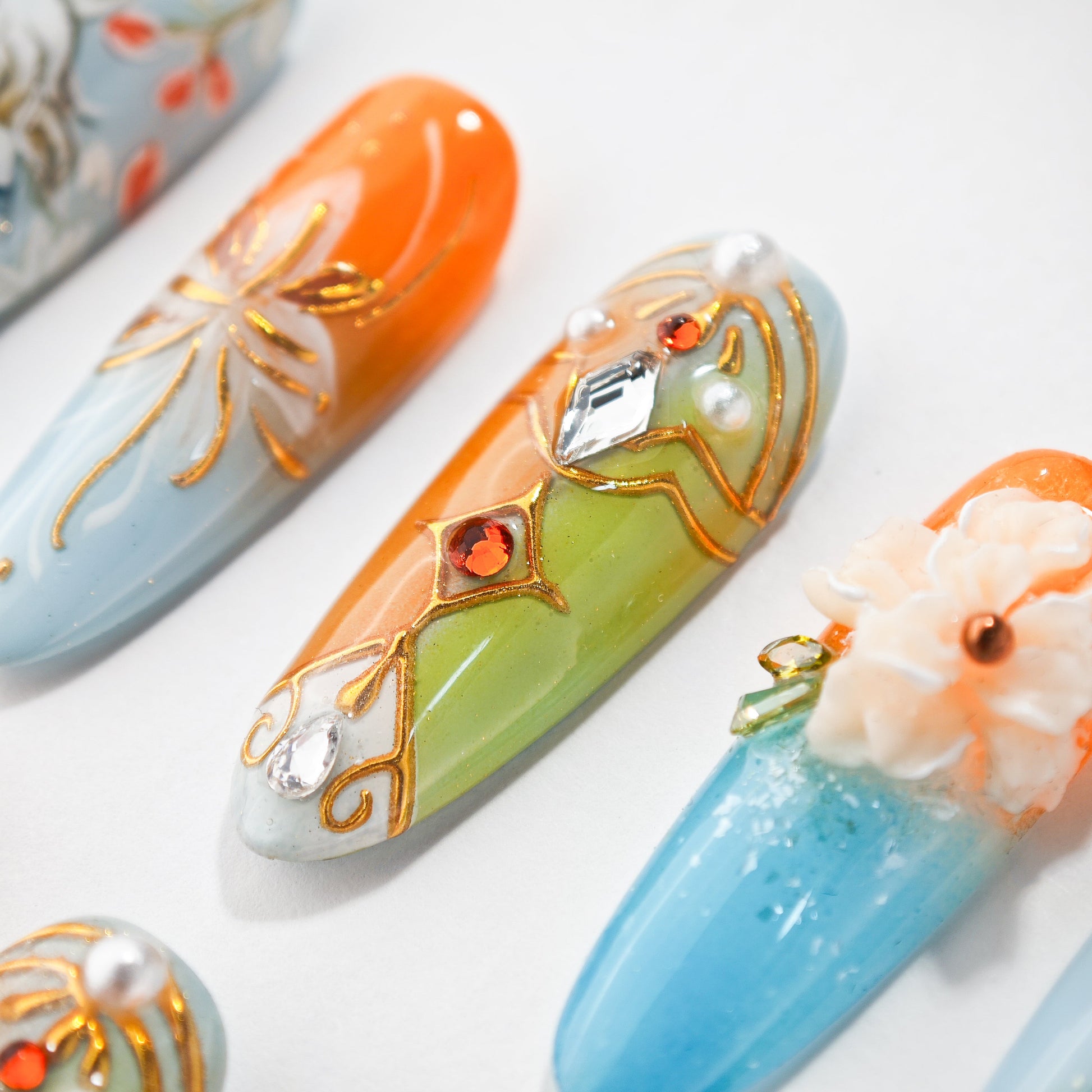 Handmade press-on nails with orange, blue, and green designs, jeweled accents, and floral details.