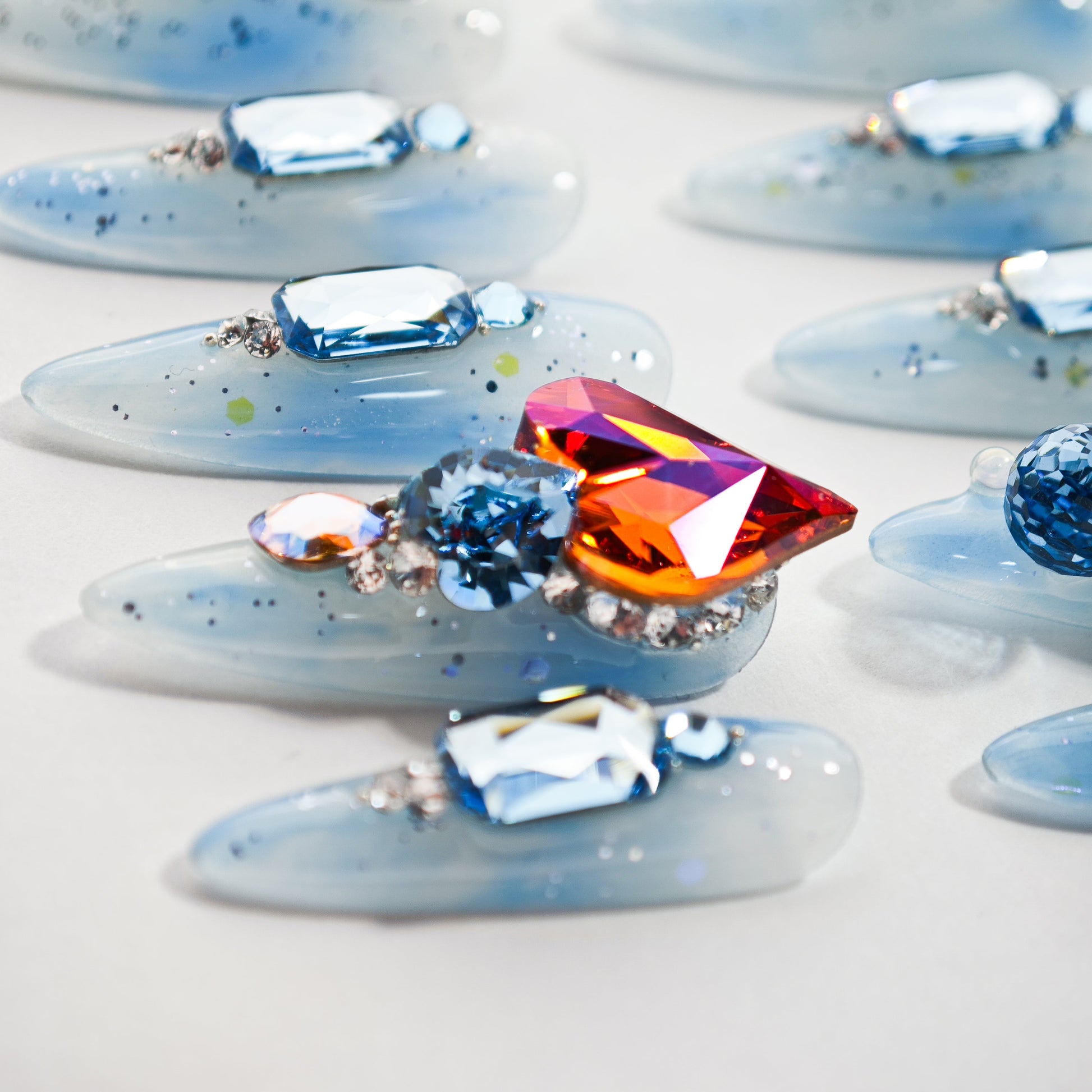 Handmade blue press-on nails with large crystal gemstones and glitter accents on a white background.