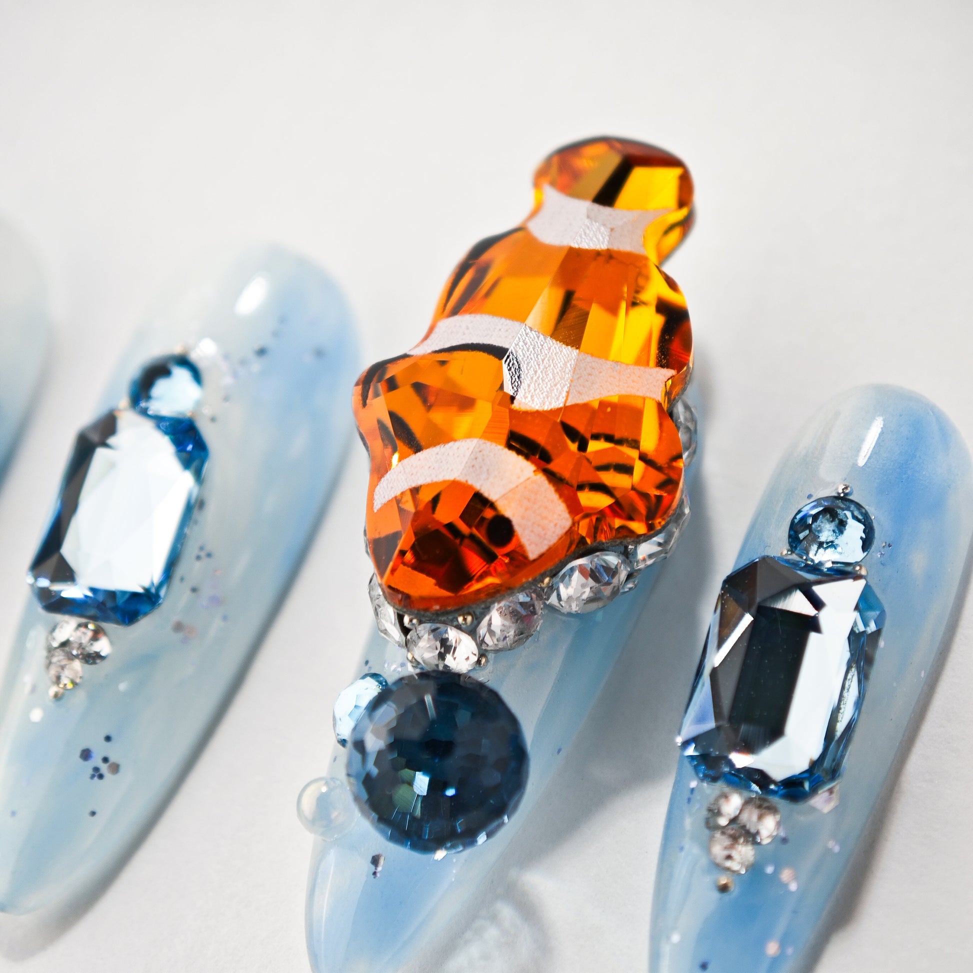 Blue press-on nails with crystal embellishments and a 3D orange fish design