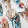 Handmade press-on nails with large gem accents, iridescent crystals, and blue glitter details.